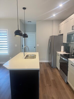 Cozinha moderna com ilha central, eletrodomésticos de aço inoxidável e iluminação pendente.