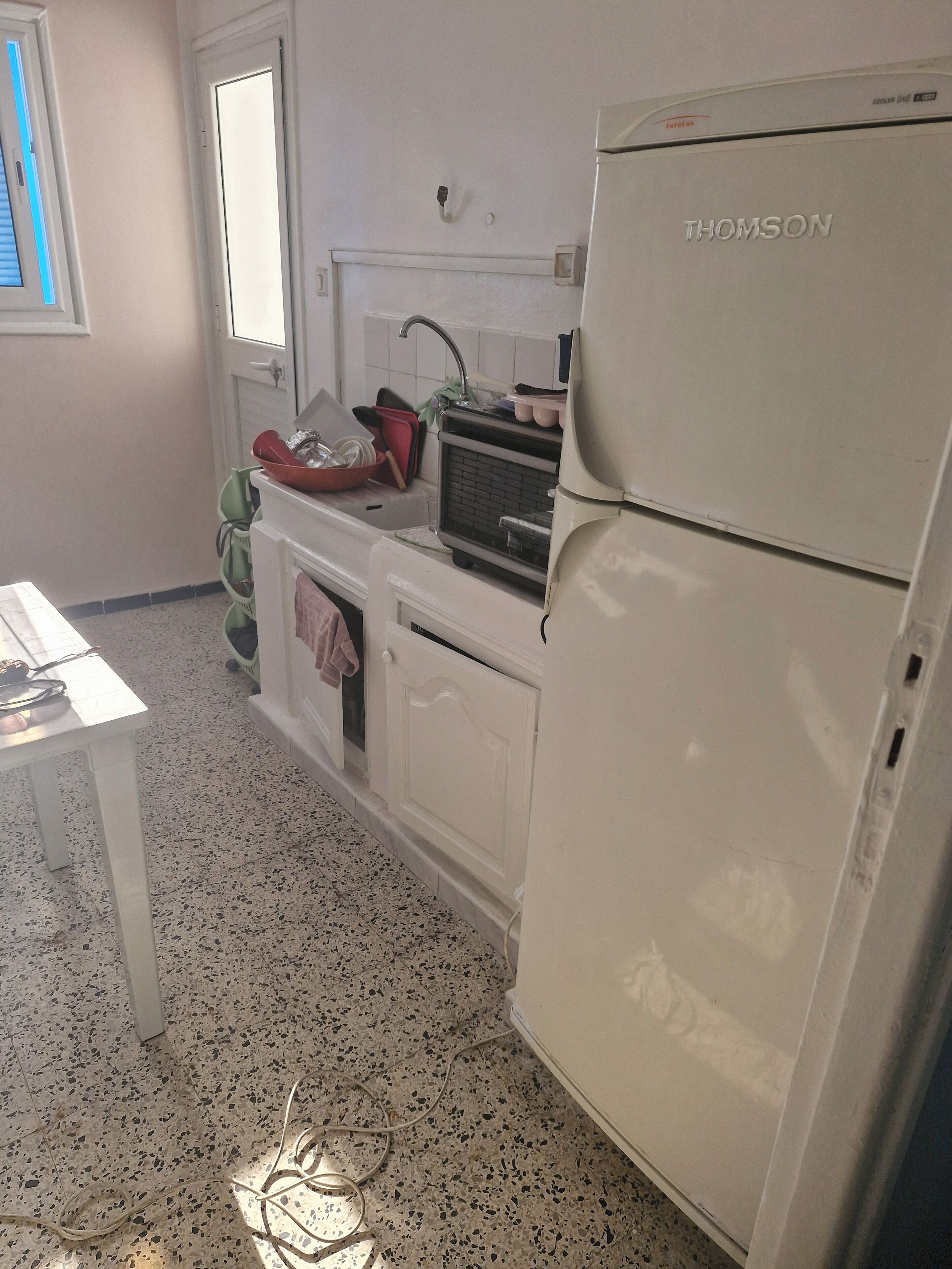 Une cuisine avec un réfrigérateur blanc, un évier et un plan de travail sur lequel se trouvent divers objets.