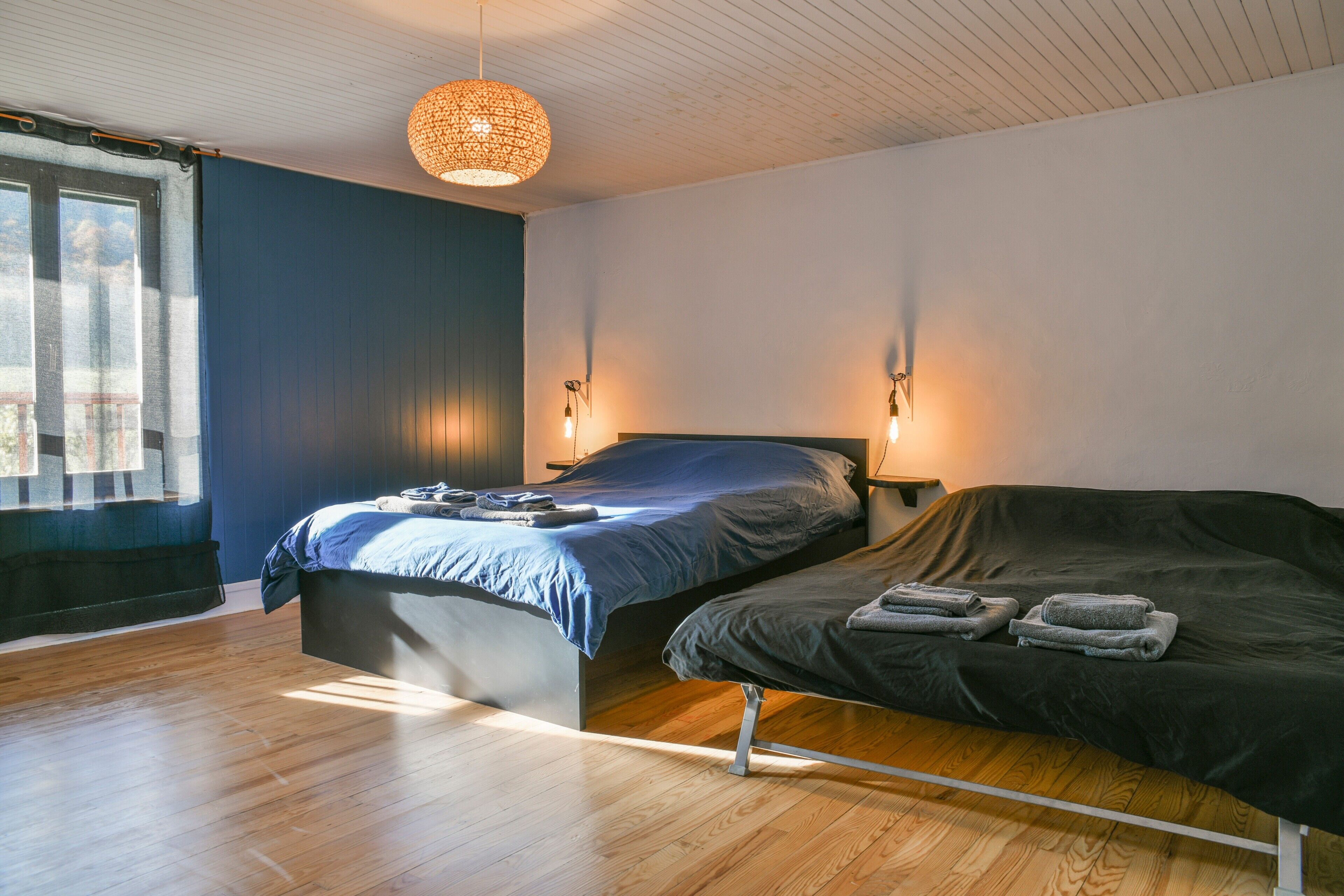Ein Schlafzimmer mit Bett, Nachttischen, einer Hängelampe und einem Fenster mit Vorhängen.