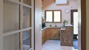 Une cuisine avec des meubles de rangement en bois, un mur d’accent en briques, une fenêtre et une horloge au mur.