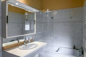 Un baño con lavamanos blanco, espejo y bañera.