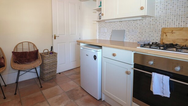 A compact kitchen with white cabinets, a small dishwasher, a gas stove, and a tiled backsplash. - Pebbles (Eastbourne)
