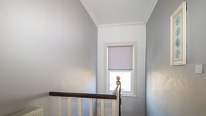 A narrow stairway with a white railing, a radiator, and a window with blinds. - Pebbles (Eastbourne)