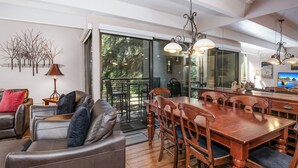 A spacious living area with a leather sofa, wooden dining table, and chairs. A large window provides a view of the outdoors. - Pool, Hot Tub, Walk to Gondola | VI111 (Vail)