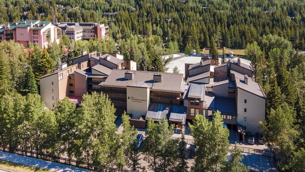 A modern hotel complex with multiple buildings, surrounded by dense forest and hills. - Pool, Hot Tub, Walk to Gondola | VI111 (Vail)