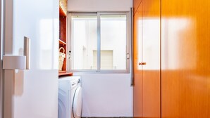 Un lavadero pequeño con lavadora, ventana y armarios de madera.