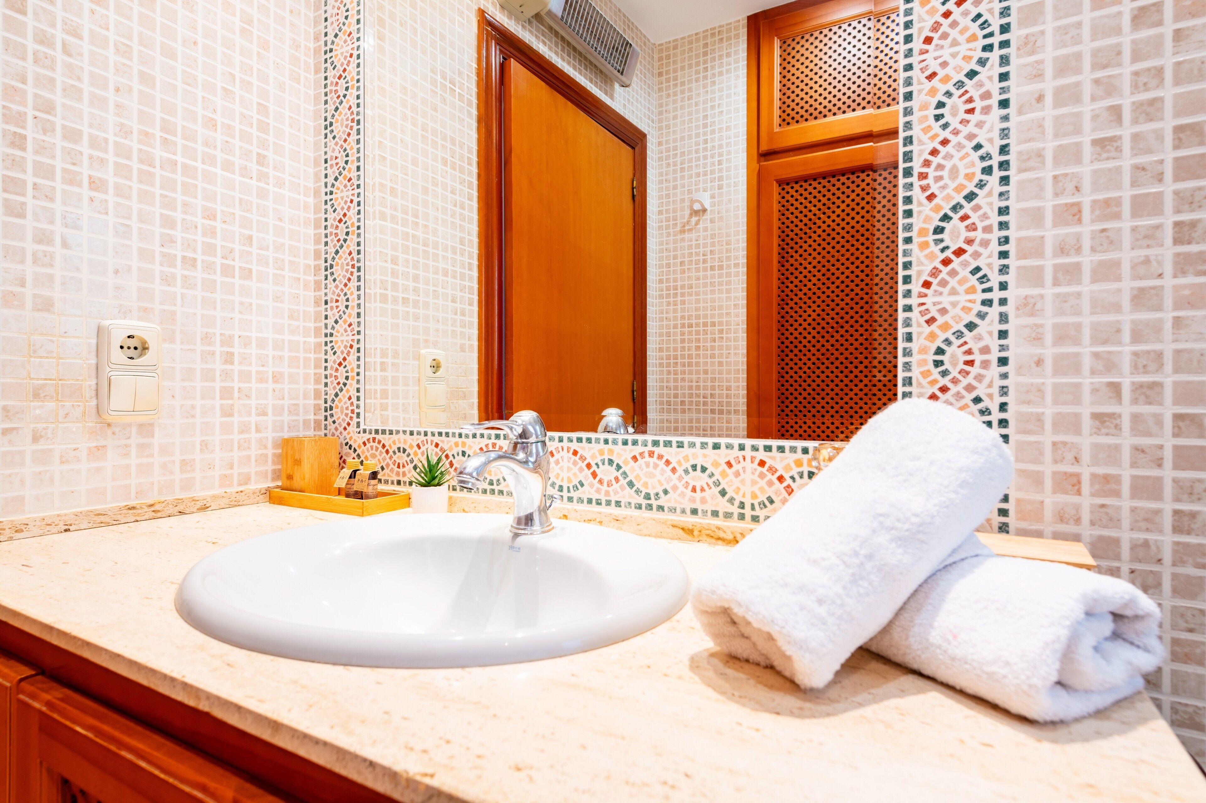 A bathroom with a sink, mirror, wooden door, and tiled walls.