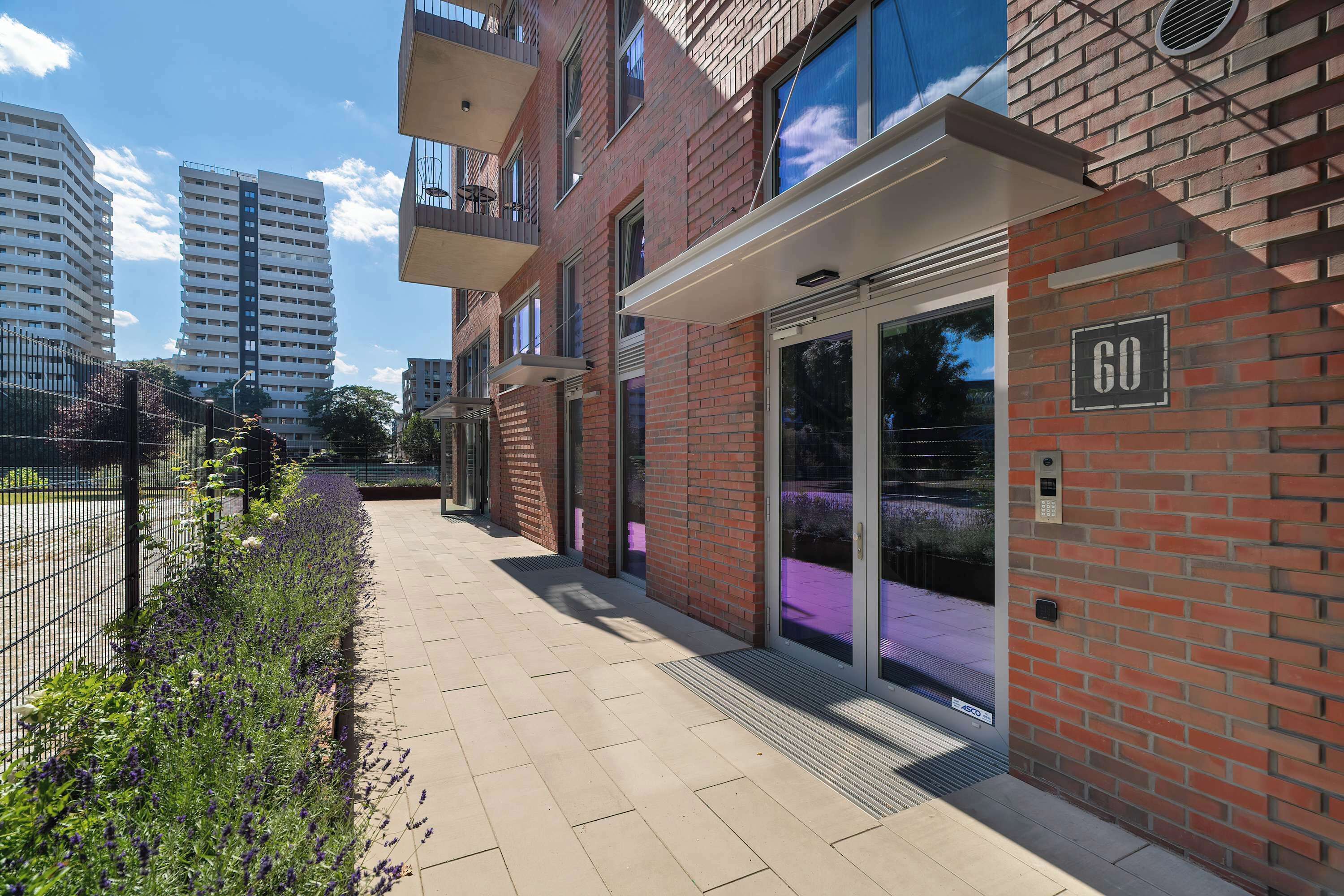 Un immeuble d’appartements moderne avec une façade en briques, de grandes fenêtres et une entrée sécurisée par un portail.