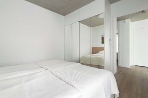 Quarto moderno com uma cama grande, um guarda-roupa com portas espelhadas e soalho de madeira.