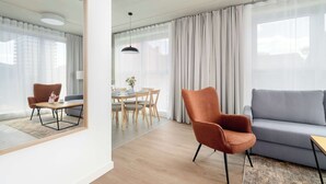 Una sala moderna con sofá, sillón, mesa de comedor y un espejo que refleja la habitación.