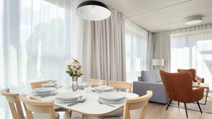 Un comedor moderno con una mesa blanca dispuesta para cuatro personas, sillas de madera y un sofá gris al fondo.