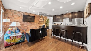 A modern kitchen with dark wooden cabinets, a stainless steel refrigerator, and a bar area with stools. - Short North Lounge - Stay for 2 (Columbus)