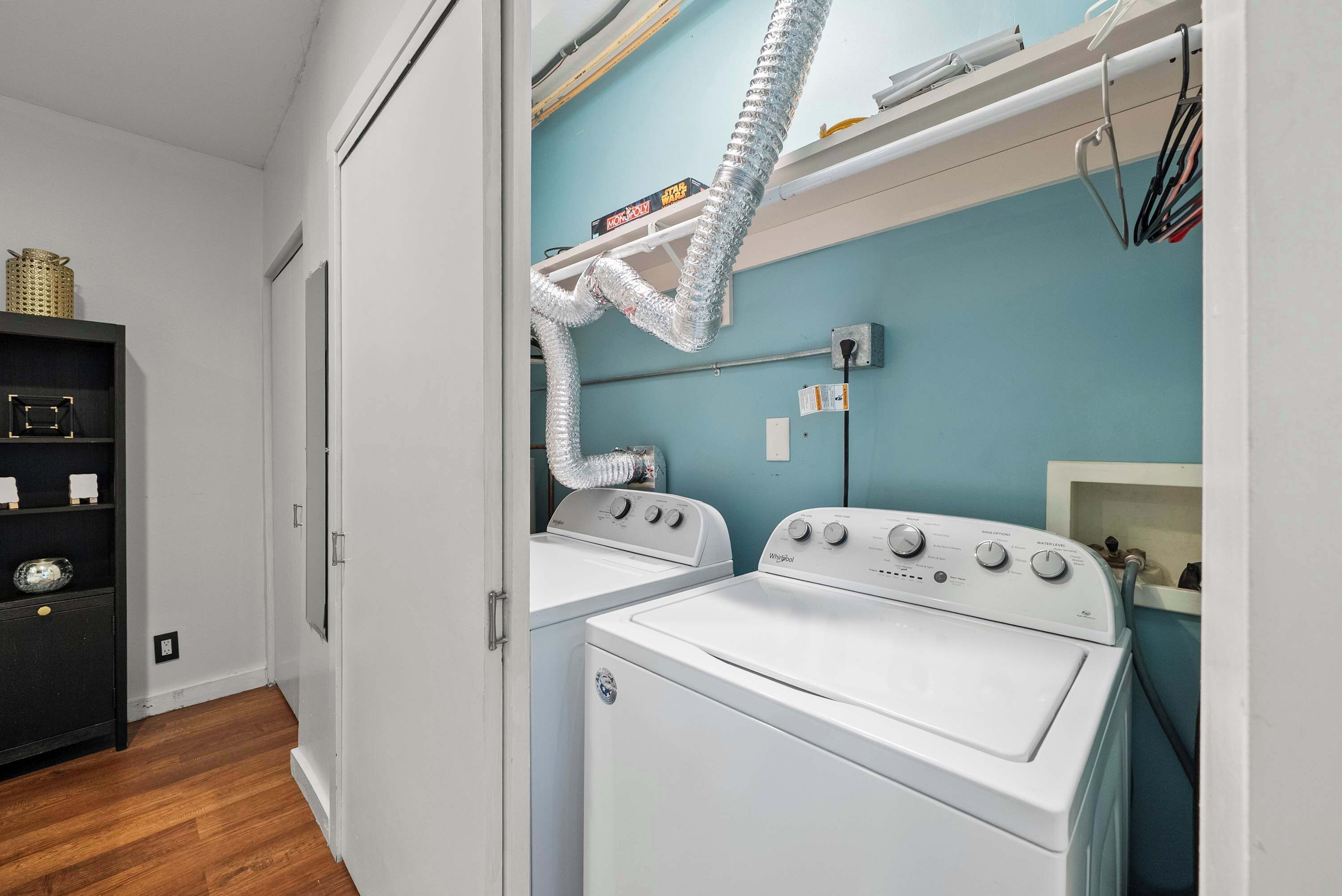 Ett tvättrum med två vita tvättmaskiner från Whirlpool, en hylla med rengöringsmedel och en ventil ovanför torktumlarna.
