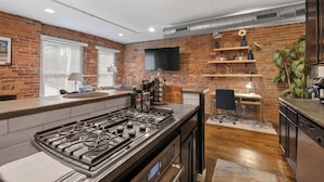 A modern kitchen with a brick wall, a flat-screen TV, and a bar area. - Short North Lounge - Stay for 2 (Columbus)