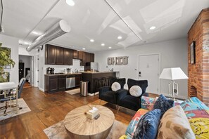 A modern living room with a sofa, coffee table, and a kitchen area in the background. - Short North Lounge - Stay for 2 (Columbus)