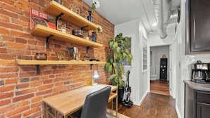 A kitchen with wooden shelves, a brick wall, and a dining area with a table and chairs. - Short North Lounge - Stay for 2 (Columbus)