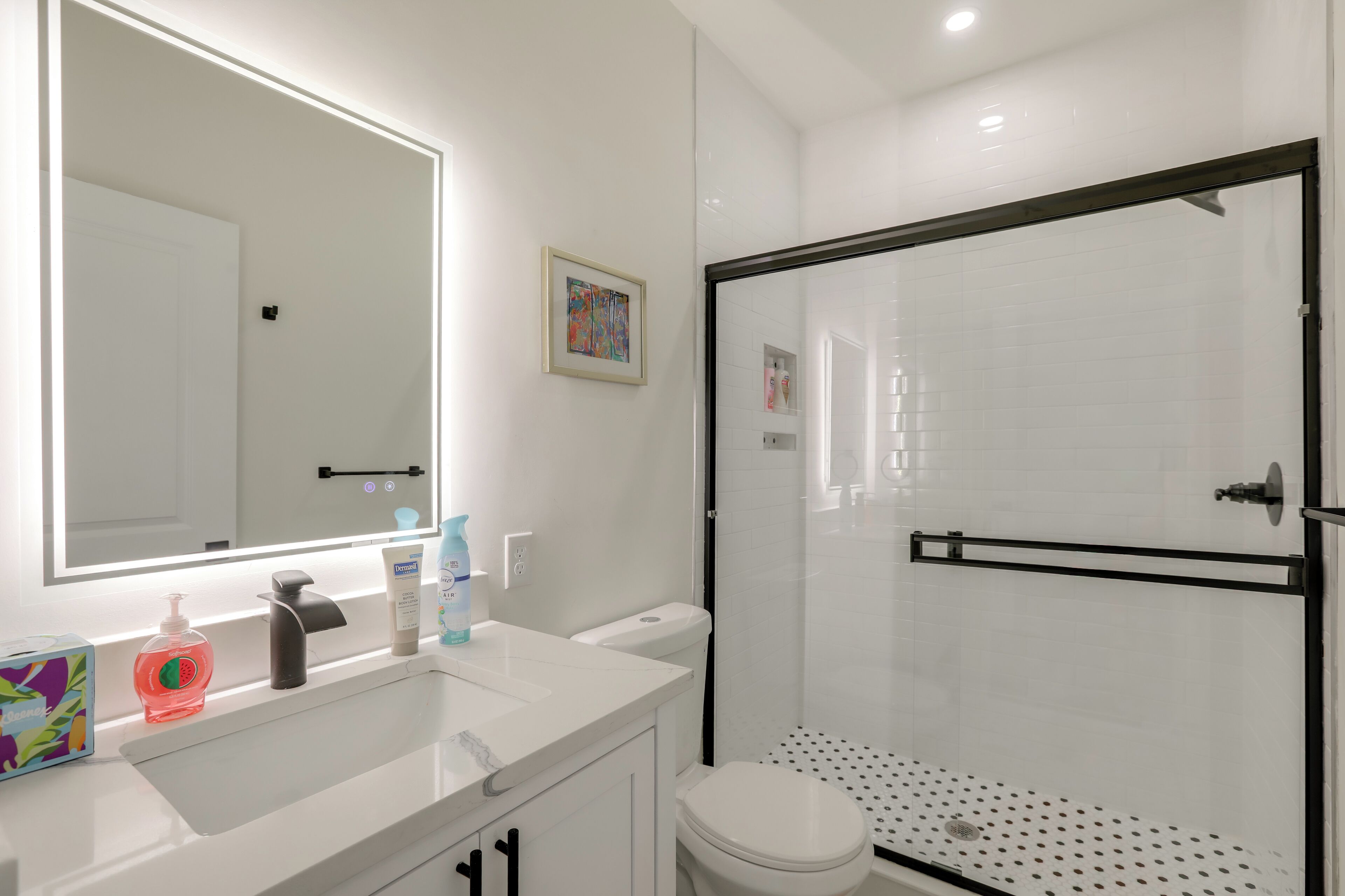 Een moderne badkamer met een wit wastafelmeubel, een grote spiegel en een douchecabine met glazen wanden.