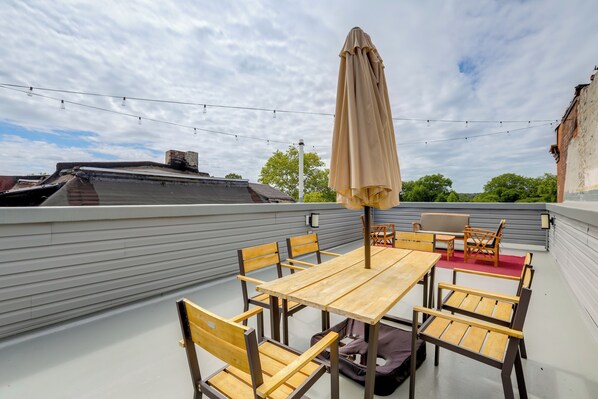 A rooftop patio with a wooden table and chairs, a beige umbrella, and string lights. - Penthouse Condo w/ Rooftop Deck in Philadelphia! (Philadelphia)