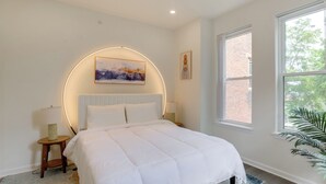 A bedroom with a bed, a round wall light, a window, and a plant. - Penthouse Condo w/ Rooftop Deck in Philadelphia! (Philadelphia)