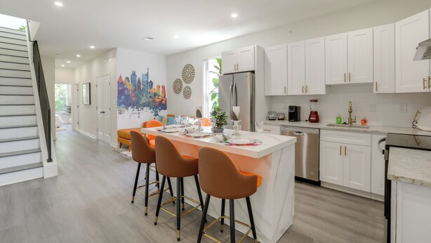 A modern kitchen with white cabinets, a central island with stools, a refrigerator, and a dishwasher. - Penthouse Condo w/ Rooftop Deck in Philadelphia! (Philadelphia)