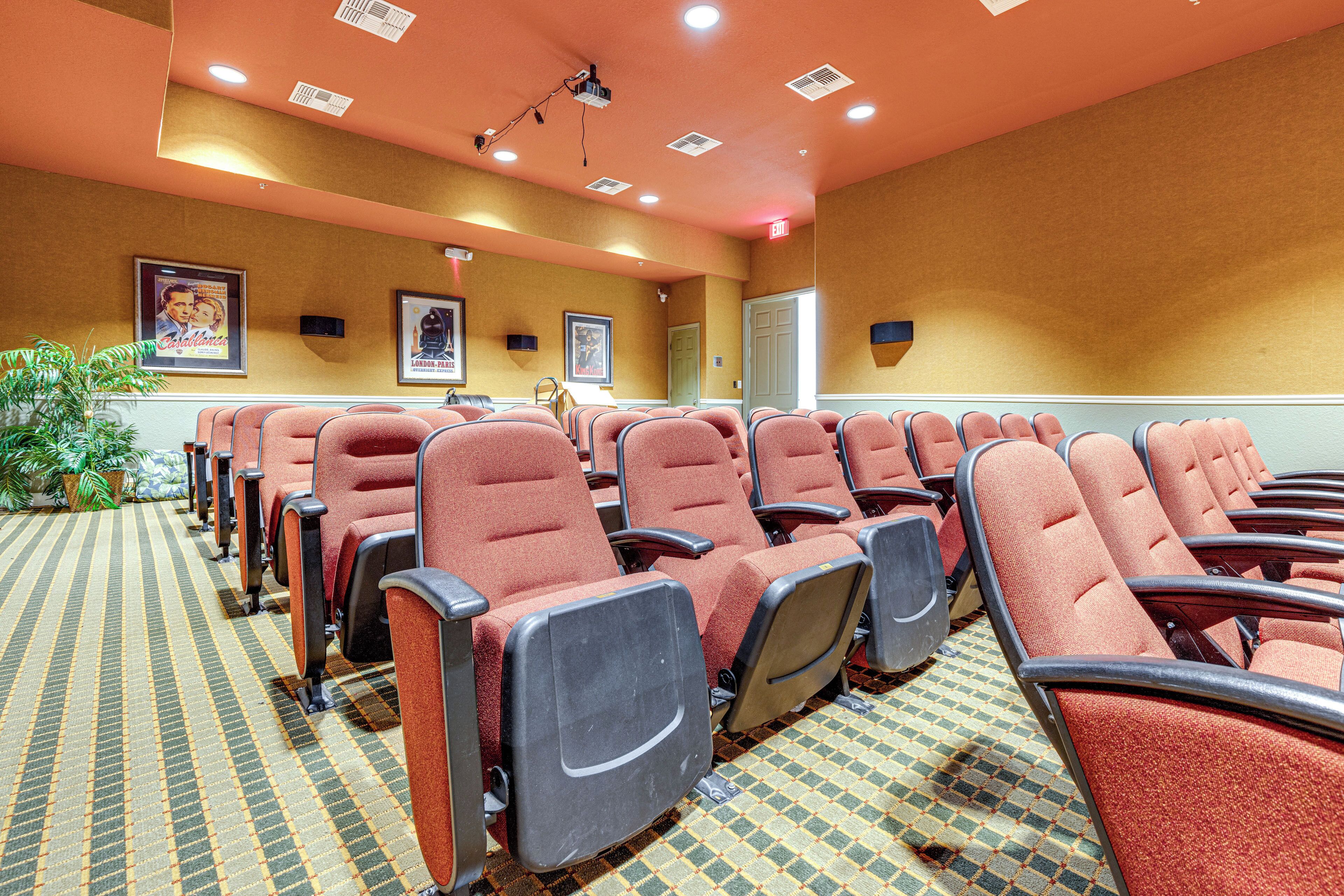 A conference room with rows of red chairs, a patterned carpet, and framed pictures on the walls.