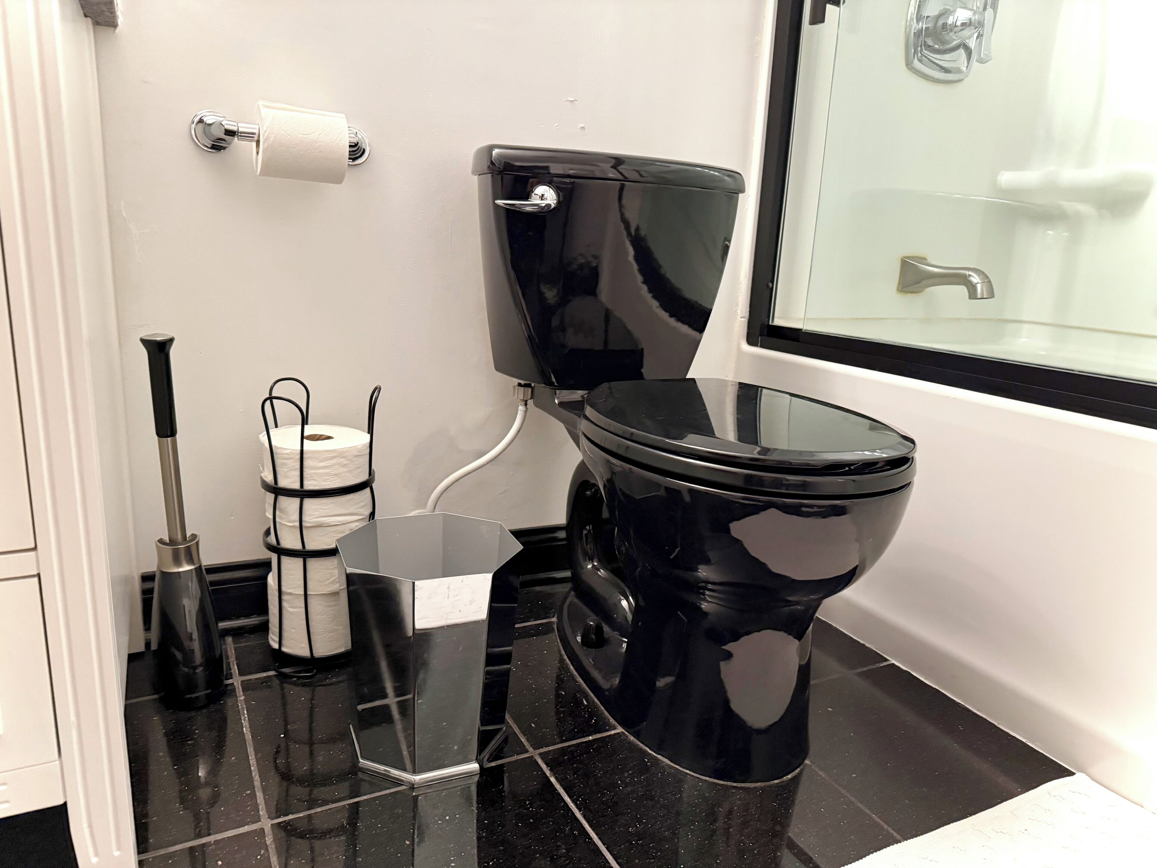 A modern bathroom with a black toilet, white walls, and a glass shower enclosure.