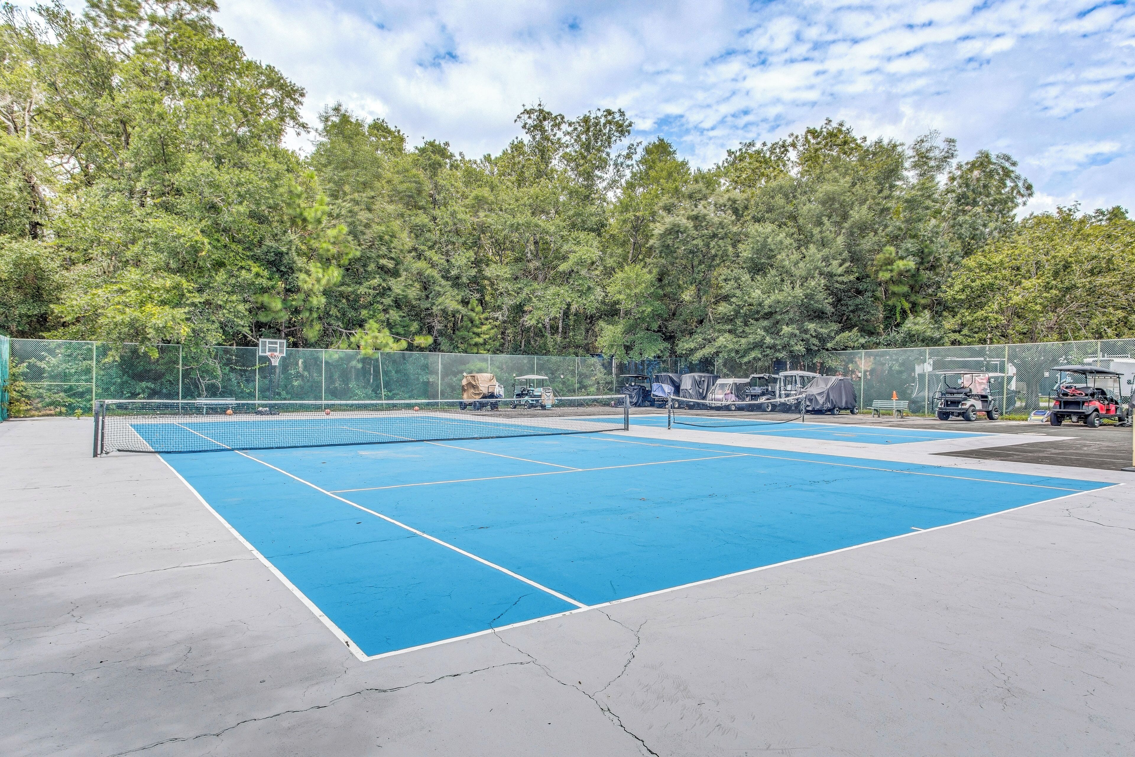 A tennis court with a net, surrounded by a green fence and trees.