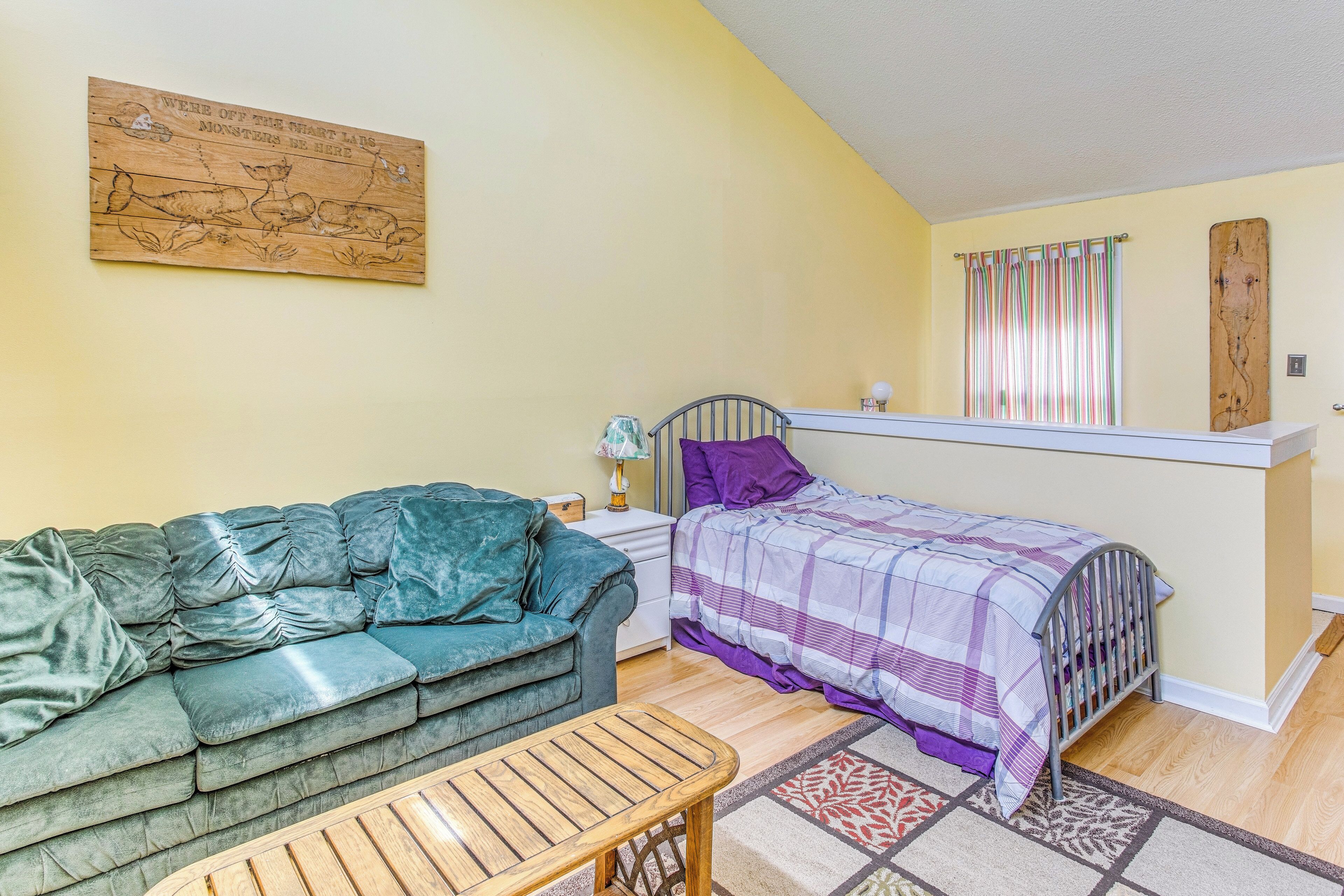 A cozy bedroom with a green sofa, a bed with a purple and white checkered bedspread, a wooden headboard, and a small table.