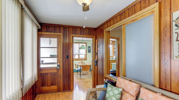 Ein Zimmer mit Holzvertäfelung, einer Couch mit gemusterten Kissen, einem großen Spiegel und einer Tür zu einem weiteren Raum.