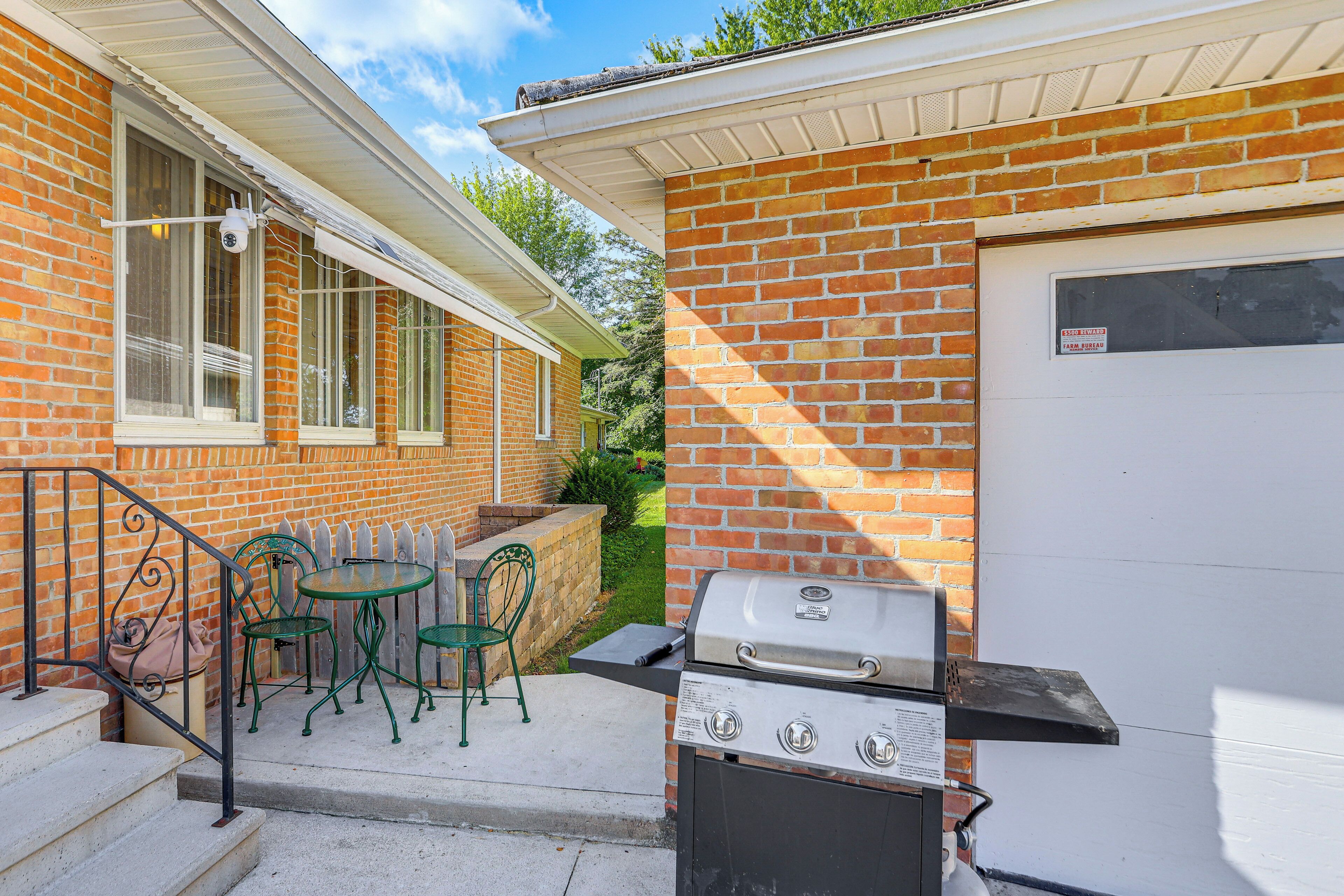 A brick house with a garage door, a grill, and outdoor seating with chairs and a table.