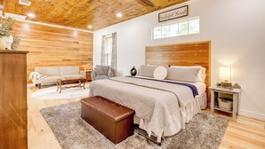 Une chambre avec un plafond en bois, un lit avec une tête de lit, une table de chevet avec une lampe et une commode.