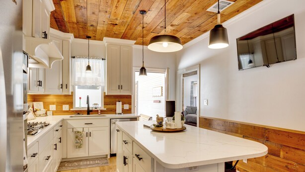 Une cuisine moderne avec des meubles blancs, un plafond en bois et un îlot central.