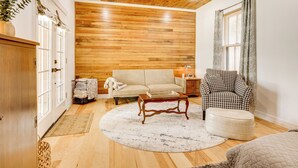 Un salon chaleureux avec un plafond en bois, un canapé beige, un fauteuil à motifs et une table basse ronde.