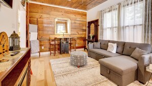 Un salon chaleureux avec un plafond en bois, un canapé, un pouf à motifs et un coin repas comprenant une table et des chaises.