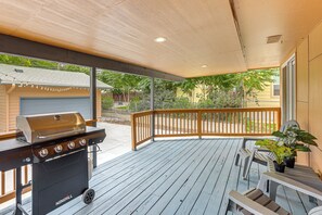 A covered outdoor patio with a barbecue grill, a wooden deck, and a view of a residential area.