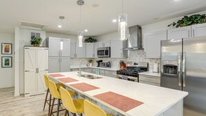 A modern kitchen with a central island, stainless steel appliances, and yellow bar stools.