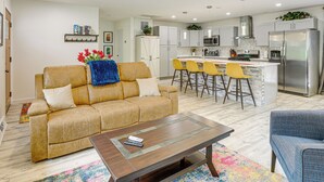 A modern living room with a sofa, a coffee table, and a kitchen area with a bar and seating.
