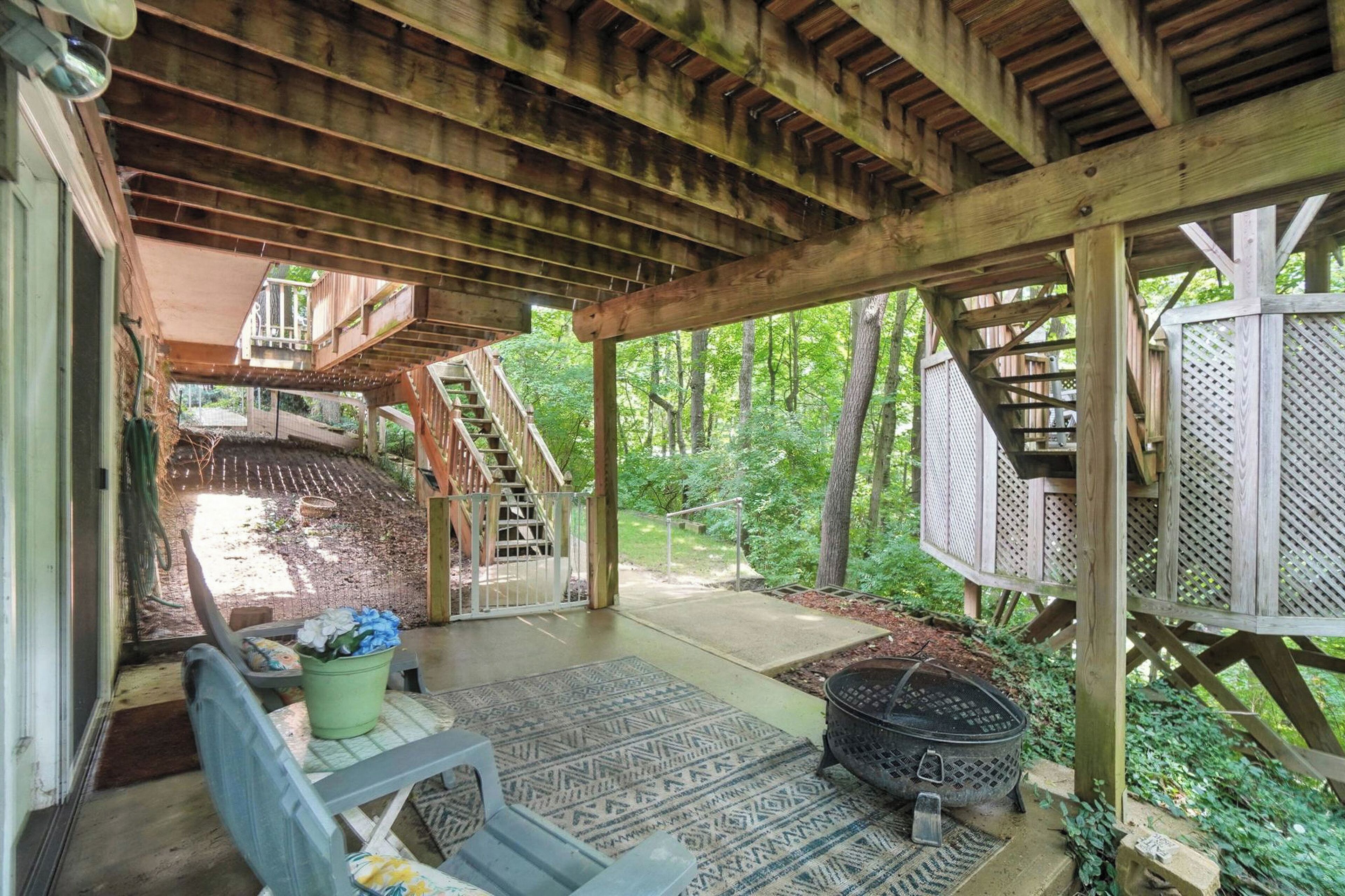 A covered wooden deck with a staircase leading to a second level, surrounded by lush greenery.