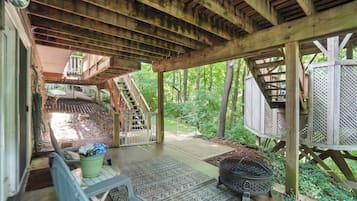 A covered wooden deck with a staircase leading to a second level, surrounded by lush greenery.