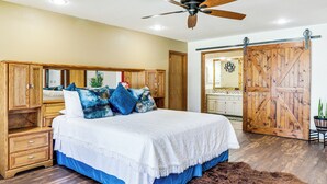 Een slaapkamer met een groot bed, een houten hoofdbord, een plafondventilator en een schuifdeur in boerderijstijl.