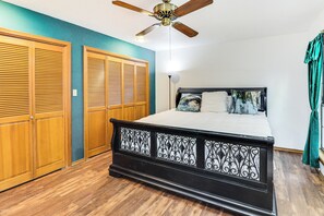 Un dormitorio con cama, armarios de madera, ventilador de techo y cortina verde.