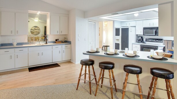 A modern kitchen with white cabinets, a large island with stools, and a microwave. - Fishing Dock & Fire Pit! Gulf Cove Group Getaway (Port Charlotte)