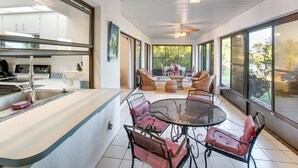 A modern kitchen with a large island, dining area with wicker chairs, and large windows offering a view of the outdoors. - Fishing Dock & Fire Pit! Gulf Cove Group Getaway (Port Charlotte)