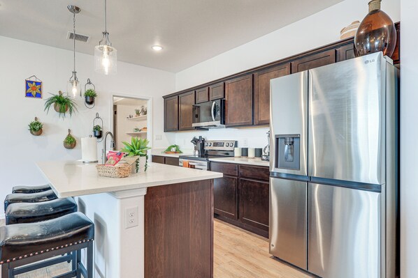 Una cocina moderna con electrodomésticos de acero inoxidable, armarios de madera y una isla central con taburetes de bar.