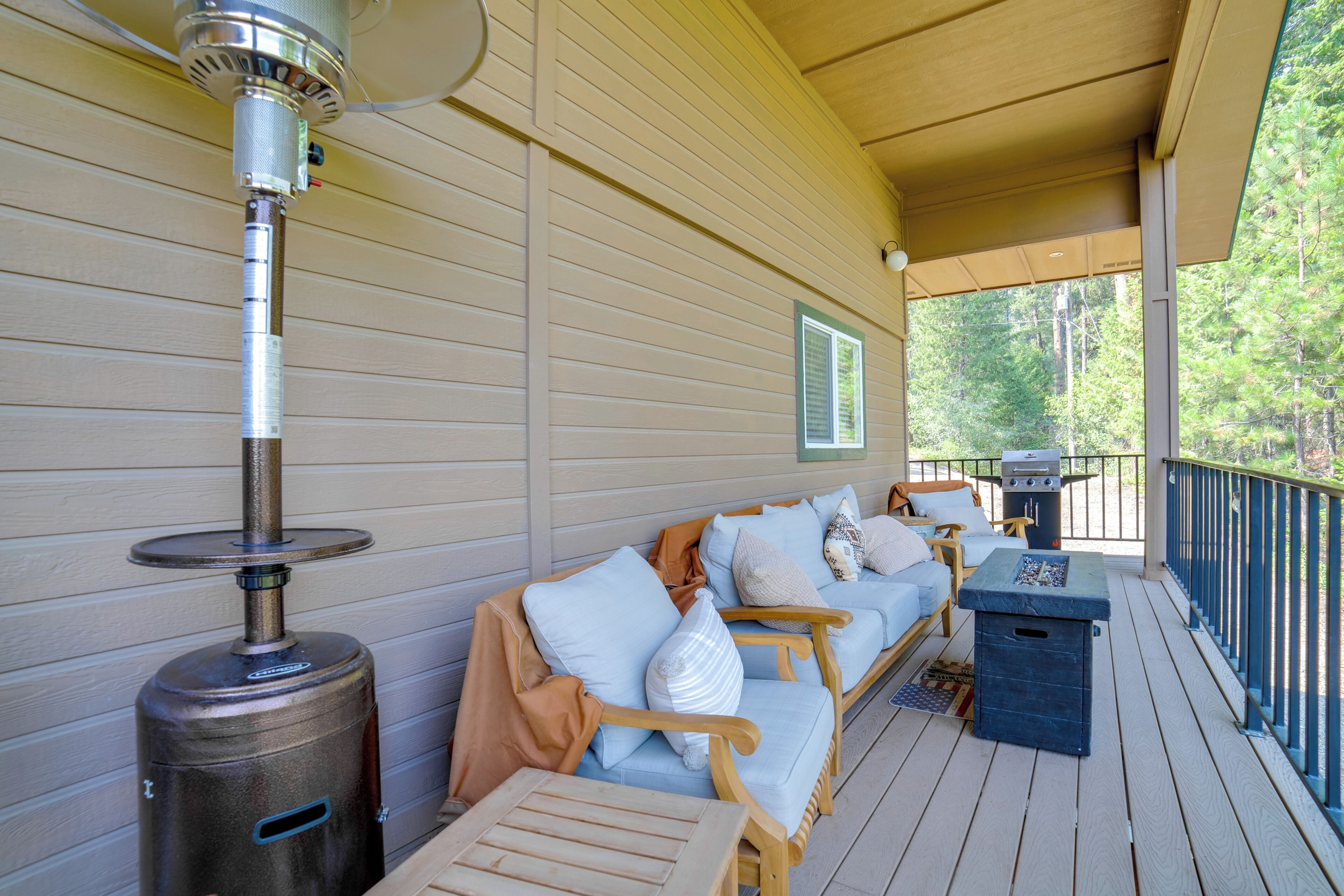 A covered porch with a wood-burning stove, outdoor seating with cushions, and a grill.