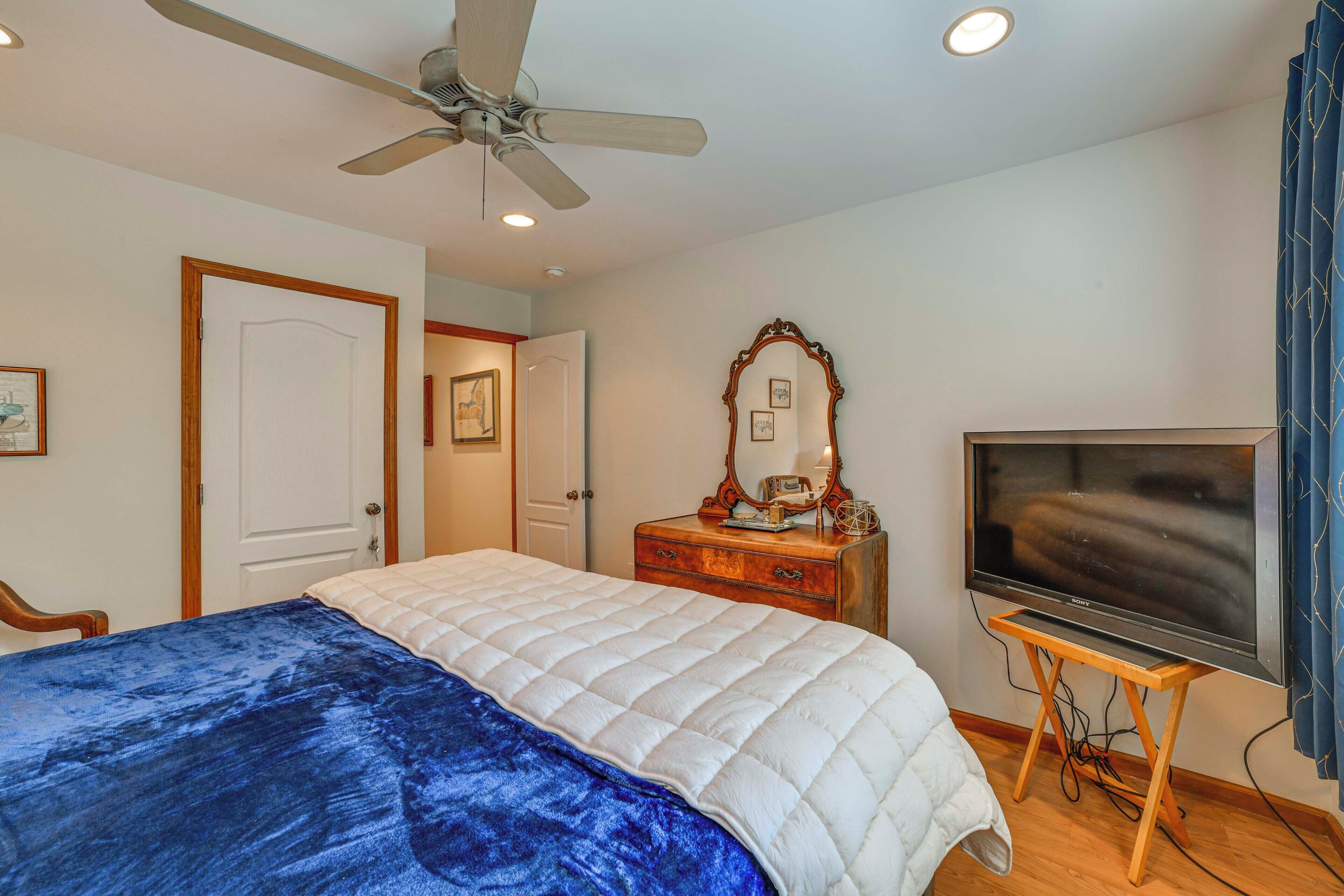 A bedroom with a bed, a ceiling fan, a TV on a wooden stand, a dresser, and a mirror.