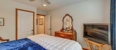 A bedroom with a bed, a ceiling fan, a TV on a wooden stand, a dresser, and a mirror.