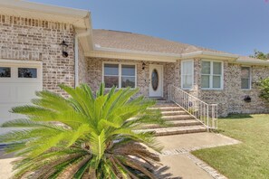 A two-story brick house with a front porch, a palm tree, and a small staircase leading to the front door.
