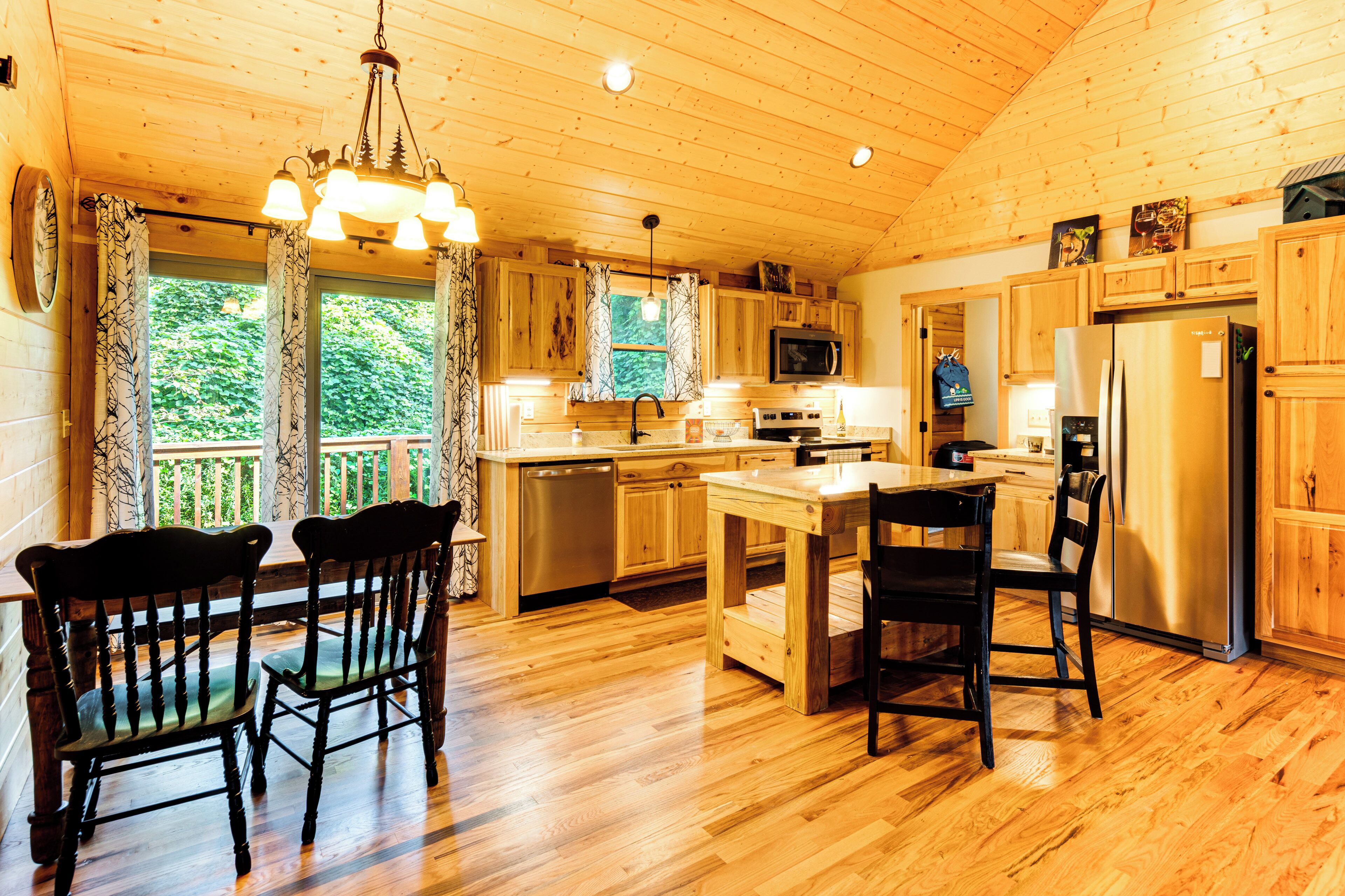 Cocina de cabaña de madera con una isla central, armarios de madera, un refrigerador de acero inoxidable y un comedor con sillas.