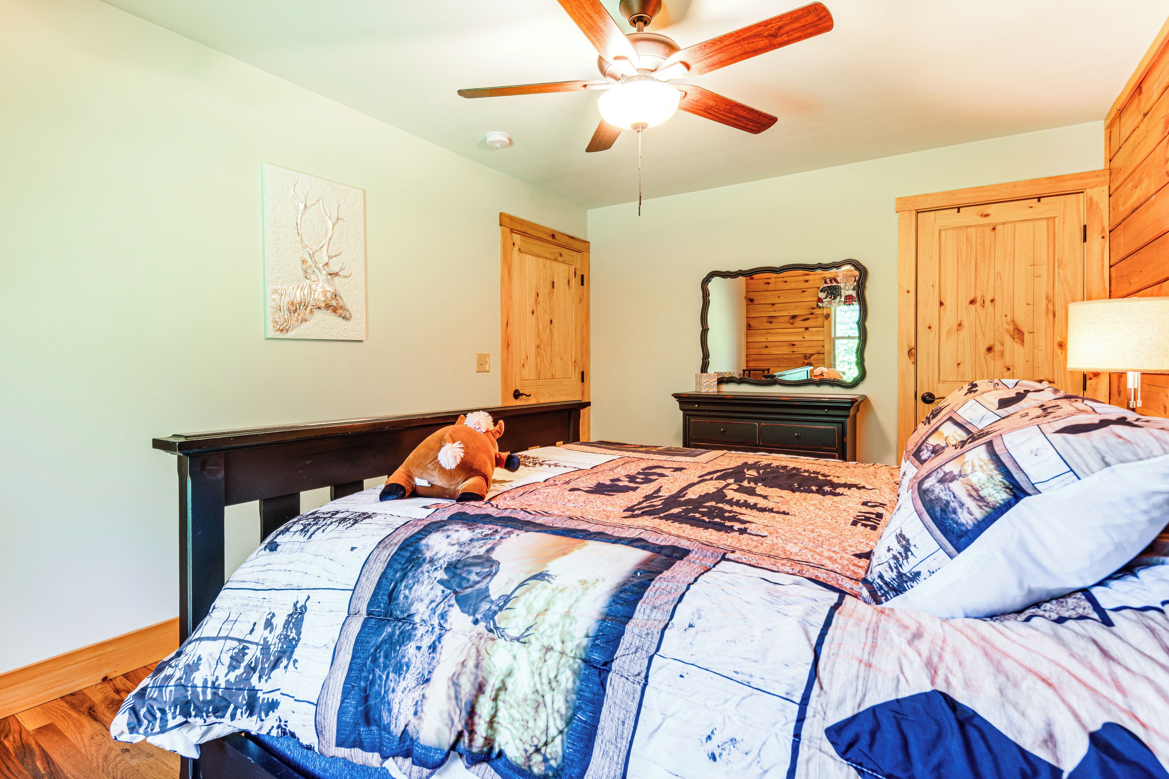 A bedroom with a bed, a ceiling fan, a wooden door, a dresser, and a mirror.